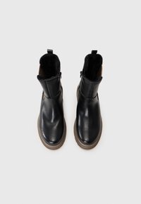 Bottines en cuir noir avec une semelle en caoutchouc texturé brun, fermeture éclair, et une doublure en fausse fourrure douce le long du bord supérieur.