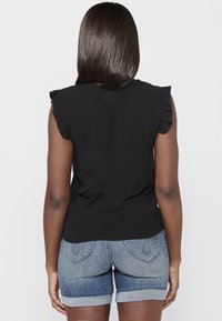Schwarzes ärmelloses Oberteil mit Rüschendetails an den Schultern, kombiniert mit Denim-Shorts mit umgeschlagenem Saum. Schlichte Stofftextur und lässiges Design.