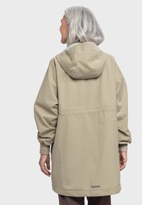 Beige wasserdichte Jacke mit Kapuze, elastischen Bündchen und tailliertem Schnitt. Hat einen grauen Akzent am Saum und eine glatte Textur.
