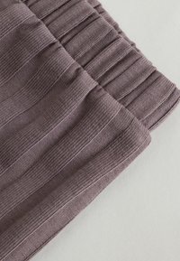 Gros plan sur un tissu tricoté côtelé plié de couleur violet doux avec des rayures verticales texturées sur un fond clair.