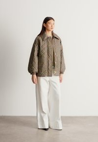 Prošívaná bunda s kostkovaným vzorem, vybavená velkým límcem a balónovými rukávy, nošená přes světlý svetr a kombinovaná se širokými bílými kalhotami.