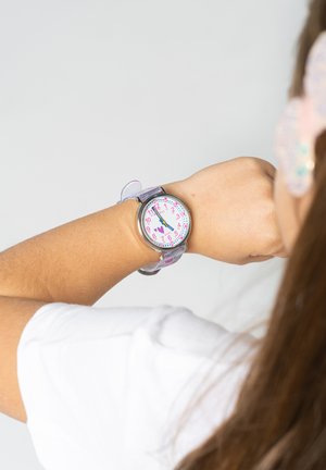 Montre analogique avec un cadran rose, un bracelet transparent et des marqueurs d'heure colorés. Les détails remarquables incluent un motif en forme de cœur sur le cadran.