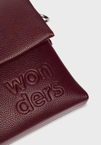 Bordowa skórzana torba o teksturowanej powierzchni, z wytłoczonym logo "wonders". Posiada zapięcie na klapkę i metalowe okucia.