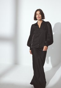 Black satin blouse with puffed sleeves and collar, paired with a long black satin skirt. Smooth texture, elegant draping.