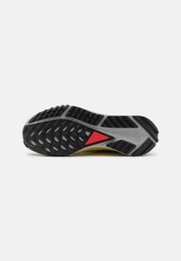 Suola di sneaker Nike con una base in gomma nera a motivo, una intersuola grigia e un triangolo rosso come accentuazione. Il design si concentra su trazione e durabilità.