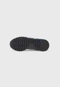 Semelle de chaussure en caoutchouc noir avec une texture ondulée ; présente des rainures pour l'adhérence et un logo au niveau du talon. Accent principalement bleu dans le design.