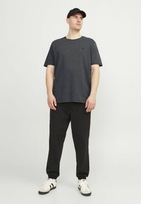 Donkergrijze korte mouwen t-shirt, zwarte joggers met accentpanelen en witte sneakers met zwarte accenten; een strak ontwerp met een relaxte pasvorm.