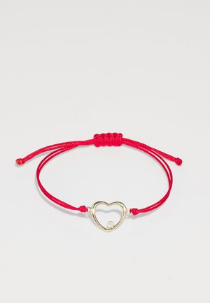 Red cord bracelet featuring a gold heart-shaped charm with an inset clear stone, secured with adjustable knots on either side.