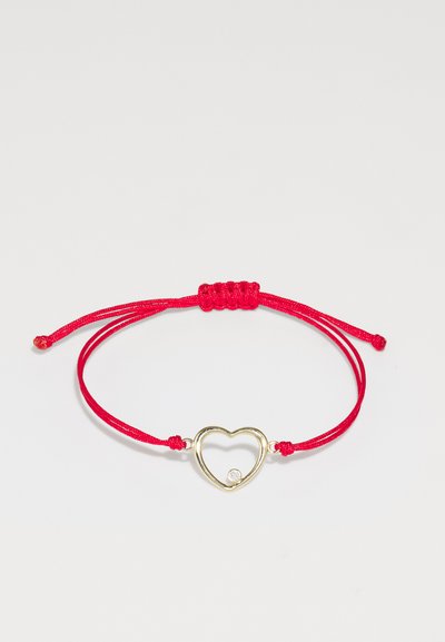 Pulsera de cordón rojo con un charm en forma de corazón dorado que tiene una piedra clara incrustada, asegurada con nudos ajustables a cada lado.