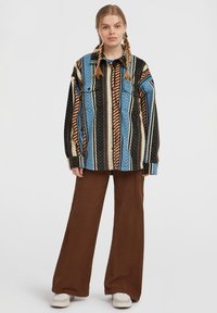 Striped jacket in blue, brown, and black; button-up design with two chest pockets; paired with brown wide-leg pants and white shoes.
