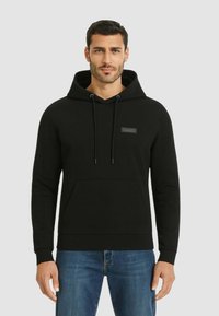 Hoodie nero realizzato in morbido tessuto testurizzato. Presenta una tasca frontale, cappuccio con lacci e una piccola etichetta con il marchio sul petto.