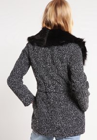 Abrigo de mezcla de lana en blanco y negro texturizado con un cuello de piel sintética negra; silueta ajustada con un detalle de cinturón en la cintura.