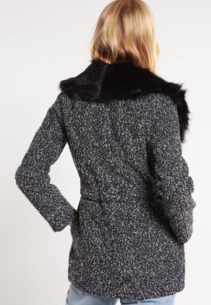 Getextureerde zwart-witte wolmix jas met een zwarte nepbont kraag; aansluitende silhuet met een riemdetail op de taille.