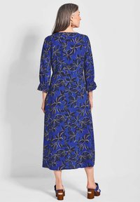 Lungo vestito floreale blu con motivi neri a foglia. Presenta maniche a tre quarti con bordi arricciati e una linea dritta fino alla caviglia.