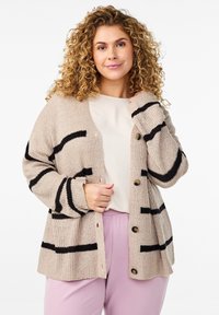 Bež prugast pleteni kardigan z črnimi črtami, z gumbnim zapiranjem in rebrastimi manšetami. Obučen čez svetlo obarvano majico in vijolične hlače.