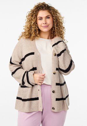 Cardigan de punto beige con rayas negras, con cierre de botones y puños acanalados. Usado sobre una blusa de color claro y pantalones morados.