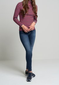 Röd och marinblå randig långärmad turtleneck topp i kombination med mörkblå skinny jeans och svarta träningsskor. Har en figurnära design.