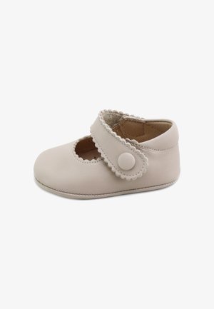 Zapato de bebé suave beige con bordes festoneados, una correa de velcro con un botón redondo y una textura lisa de cuero.