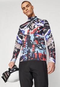 Langarmtrui met een hoge kraag, met een levendig abstract patroon in zwart, rood, blauw en beige. Het materiaal lijkt rekbaar en textuur te hebben.