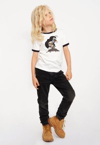 White short-sleeved t-shirt with blue trim, featuring a cartoon mole graphic. Paired with dark jeans and brown lace-up boots.
