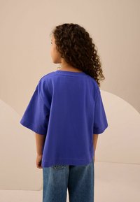 Camiseta de algodón morada con mangas cortas y anchas, y un corte relajado, combinada con jeans de mezclilla azul claro. Textura suave, sin patrones visibles.