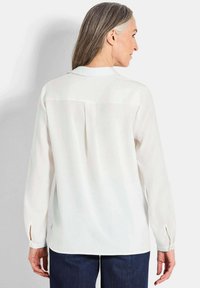 Witte blouse met lange mouwen en kraaghalslijn, voorzien van een plooi aan de achterkant en met knoopmanchetten, gecombineerd met donkerdenim broek.