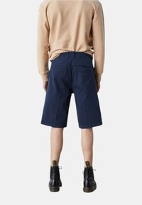 Pantaloni corti blu navy realizzati in tessuto resistente, con un taglio dritto, dotati di tasche posteriori e indossati con stivali neri alla caviglia.
