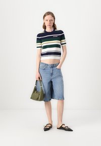 Maglione corto a righe in blu navy, verde e bianco; pantaloni Bermuda in denim azzurro chiaro; borsa verde oliva; scarpe ballerine nere a punta.
