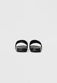 Fekete csúszó szandálok nyitott orral, puha, textúrált anyagból, dupla oldalszíjjal és lapos talppal. Minimalista és áramvonalas forma.