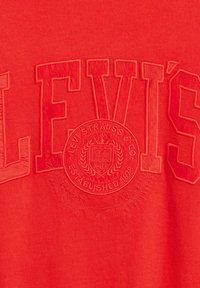 Rode katoenen T-shirt met verhoogde letters, "LEVI'S," met een cirkelvormig logo in het midden, reliëfdetails en een gladde textuur.