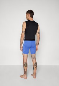 Sort med ermer og rund hals, kombinert med blå treningsshorts med et tettsittende design og synlige sømmer.