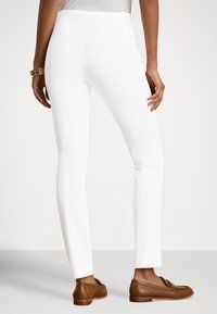 Fehér, testhez simuló nadrág sima textúrával és enyhe rugalmassággal. Klasszikus kialakítású, közepes derékmagassággal és karcsú nadrágszár sziluettel.