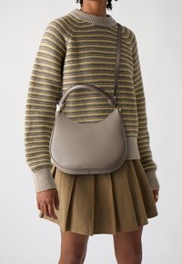 Harmaa nahkainen käsilaukku pyöreällä siluetilla, sileällä tekstuurilla, yläkahvalla ja irrotettavalla olkahihnalla. Yhdistetty raidalliseen neulepuseroon ja hameeseen.