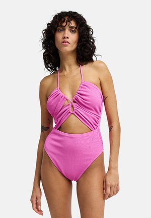 Roze geribd badpak met halterbandjes, gedraaide voorkant en open zijkanten. Voorzien van een cirkelvormig accent in de taille en hoge beenopeningen.
