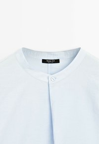 Chemise blanche à col avec un seul bouton près de l'encolure, avec une étiquette "Massimo Dutti" à l'intérieur du col.