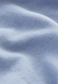Tejido de punto azul claro con una textura suave, que presenta variaciones sutiles y patrones finos en toda la superficie.