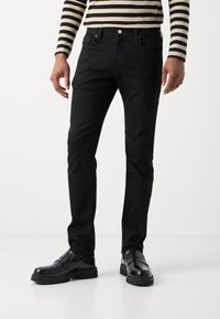 Sorte denimjeans har en smal passform med tradisjonell fem-lommestil. Brukt med en stripete langermet skjorte og svarte loafers.