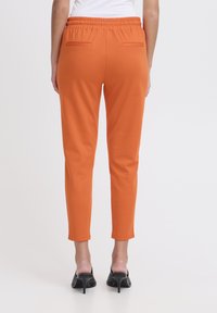 Pantalones de chándal naranja con un corte relajado, que cuentan con una cinturilla elástica fruncida y dos bolsillos traseros. Textura suave y diseño de pierna ajustada.