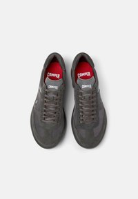 Gray sneakers featuring a mix of suede and mesh materials, with a rounded toe, flat laces, and red insoles that display the "CAMPER" logo.