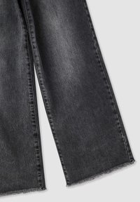 Pantaloni larghi in denim nero con una finitura sbiadita e orlo sfrangiato. Il tessuto è testurizzato con un classico design a cinque tasche.