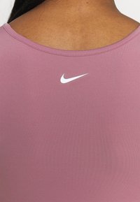 Koszulka sportowa Nike w miękkim różowym materiale o gładkiej fakturze. Posiada białe logo na górnej części pleców. Prosty, okrągły dekolt.