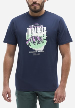 Homme portant un t-shirt bleu marine avec un graphisme de montagnes et le texte « Grandes Jorasses, Chamonix, France, Millet. »