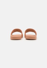 Sandales à glissière de couleur pêche avec une finition lisse, un talon ouvert et des larges sangles. Matériau doux et flexible et design minimaliste.