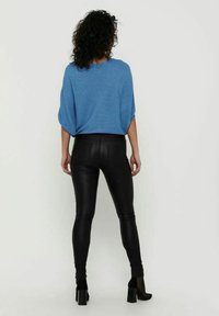 Haut bleu ample avec manches chauve-souris, associé à un legging noir moulant et brillant, et des bottines noires à talons.