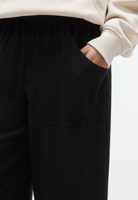 Μαύρο παντελόνι με υφή, με πλαϊνή τσέπη. Το ύφασμα είναι ελαφρύ και πέφτει απαλά. Συνδυάζεται με κρεμ φούτερ.