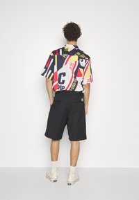 Kortærmet skjorte med et farverigt grafisk print med fede former og tekst, parret med sorte shorts og lyse sneakers.