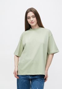 Lichtgroen oversized T-shirt van zachte katoen met een hoge halslijn en korte mouwen. Gecombineerd met spijkerbroeken.