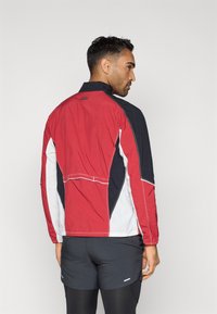 Sarkans, melns un balts vieglais apmetnis ar augstu apkakli, kontrastējošām paneļiem un elastīgām aprocēm. Iekļauts arī kabata ar rāvējslēdzēju aizmugurē.