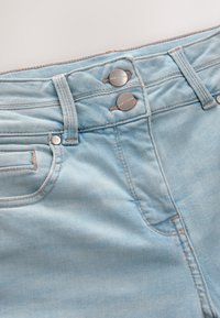 Svijetloplave traperice visokog struka s dva srebrna metalna gumba i kontrastnim šavovima duž šavova i džepova.