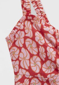 Tissu rouge avec motif floral abstrait rose et orange et bretelles froncées, montrant la partie supérieure d’un vêtement.